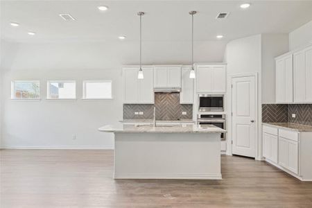 Kitchen featuring light wood-type flooring, white cabinets, a kitchen island with sink, stainless steel appliances, and decorative backsplash