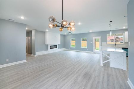 Unfurnished living room featuring a notable chandelier, light wood-type flooring, and sink