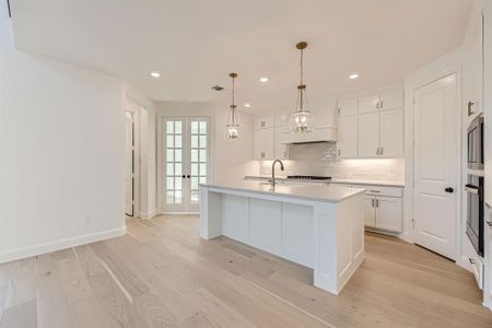 Kitchen featuring white cabinets, french doors, a kitchen island with sink, light hardwood / wood-style flooring, and appliances with stainless steel finishes