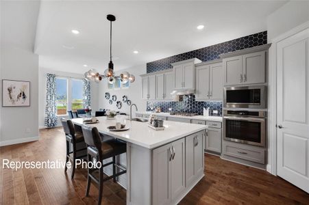 Kitchen featuring backsplash, hanging light fixtures, a center island with sink, dark wood-type flooring, and appliances with stainless steel finishes