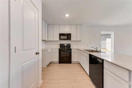 Kitchen with black appliances, sink, white cabinets, light hardwood / wood-style floors, and kitchen peninsula