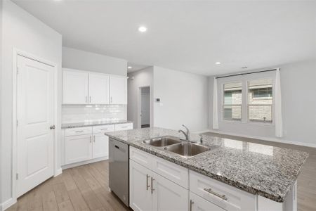 Kitchen featuring sink, white cabinetry, light stone counters, a center island with sink, and dishwasher