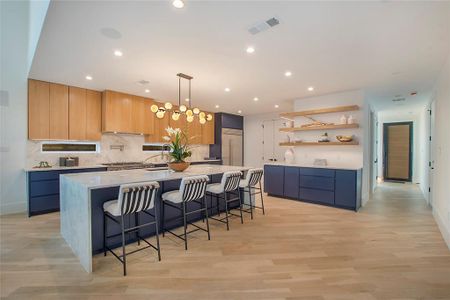 Kitchen featuring pendant lighting, a breakfast bar, light wood-type flooring, a large island, and light stone counters