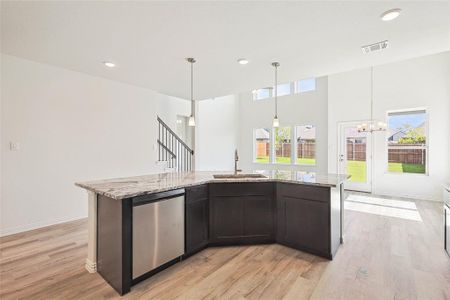 Kitchen with a chandelier, sink, dishwasher, light stone counters, and light hardwood / wood-style floors