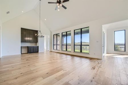 Unfurnished living room with ceiling fan with notable chandelier, light hardwood / wood-style flooring, and high vaulted ceiling