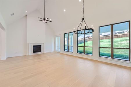 Unfurnished living room featuring high vaulted ceiling, ceiling fan with notable chandelier, and light wood-type flooring