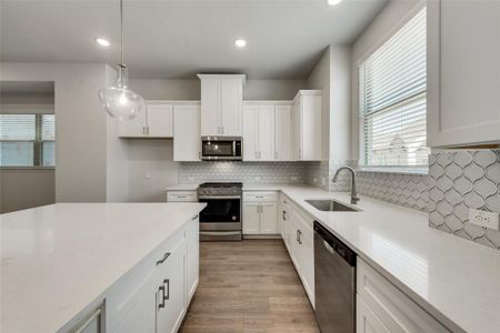 Kitchen featuring appliances with stainless steel finishes, tasteful backsplash, sink, light hardwood / wood-style floors, and white cabinetry