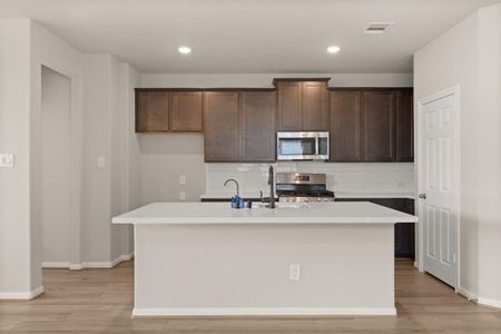 This light and bright kitchen features a large quartz island, dark stained cabinets, a large sink overlooking your family room, recessed lighting, and beautiful backsplash.