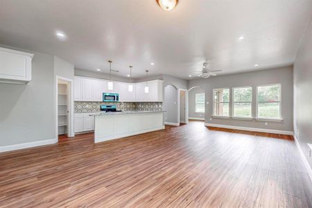 Kitchen with stove, hanging light fixtures, white cabinets, light wood-type flooring, and backsplash