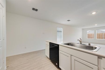 Kitchen with sink, white cabinets, light wood-type flooring, and black dishwasher