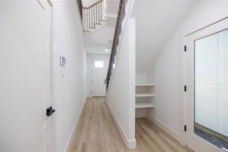 Alternate view of the front entrance showcasing the durable wood-like LVP flooring that extends throughout, ensuring long-lasting quality. Additional shelving under the staircase creates an ideal mudroom, maximizing storage and functionality. The side door offers convenient access for both residents and short-term rental guests, leading directly to a spacious 32x8 private yard.