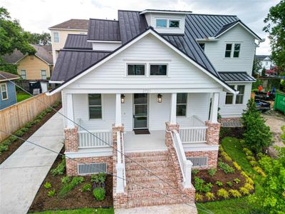 Aerial view of a white house with a striking brick entrance and a metal roof. A guy wire stretches across the front yard, to be removed.