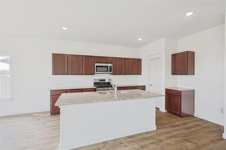 Kitchen featuring sink, light wood-type flooring, stainless steel appliances, and a kitchen island with sink