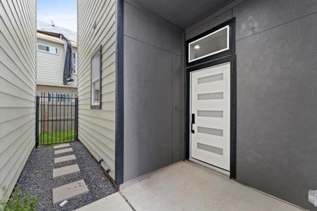 Modern entryway featuring a sleek white door with horizontal glass panels. A stepping-stone path leads to a gated fence, adding privacy and a contemporary touch.