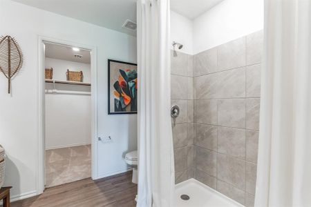 Bathroom with a tile shower, hardwood / wood-style flooring, and toilet