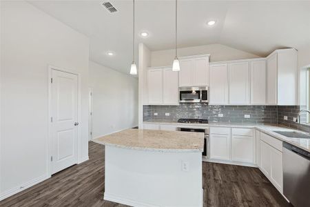 Kitchen with sink, lofted ceiling, white cabinetry, stainless steel appliances, and decorative light fixtures