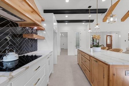 Kitchen with white cabinets, light stone countertops, pendant lighting, a center island, and stovetop