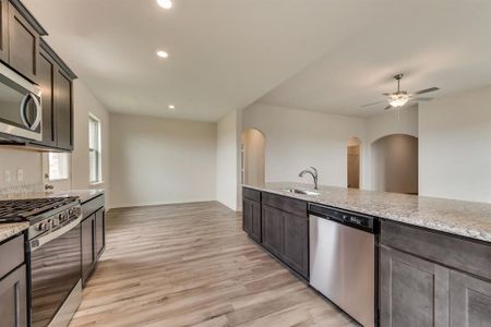 Kitchen with dark brown cabinets, light hardwood / wood-style floors, light stone countertops, appliances with stainless steel finishes, and sink