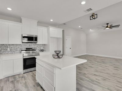 Kitchen with appliances with stainless steel finishes, ceiling fan, light hardwood / wood-style flooring, white cabinets, and a center island