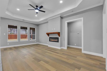 Unfurnished living room featuring ceiling fan, crown molding, a tray ceiling, and light hardwood / wood-style flooring