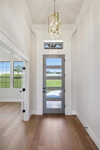 Foyer entrance with wood-type flooring, crown molding, and a chandelier