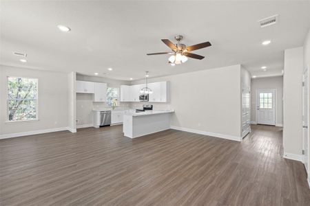 Unfurnished living room featuring sink, ceiling fan with notable chandelier, plenty of natural light, and dark hardwood / wood-style flooring