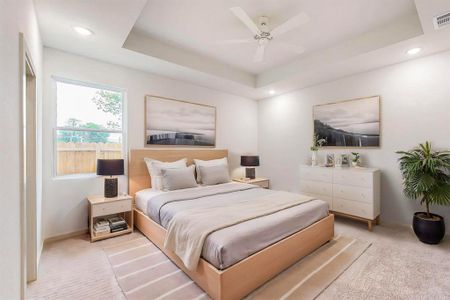 Bedroom with light carpet, ceiling fan, and a tray ceiling