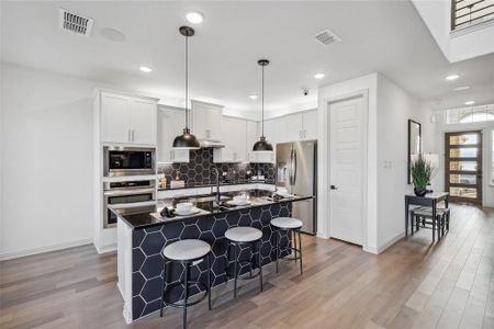 Kitchen with a breakfast bar, stainless steel appliances, tasteful backsplash, white cabinets, and a center island with sink