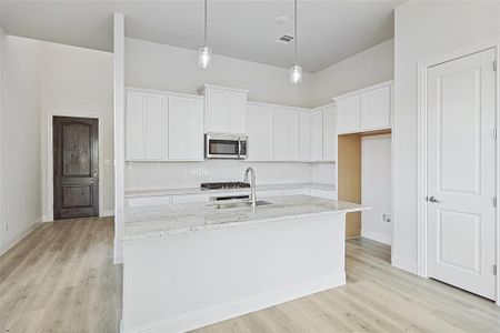 Kitchen with light stone counters, sink, white cabinets, and an island with sink