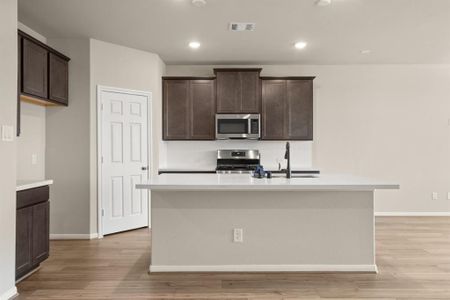 This light and bright kitchen features a large quartz island, dark stained cabinets, a large sink overlooking your family room, recessed lighting, and beautiful backsplash.