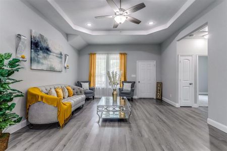 Living room featuring ceiling fan, light wood-type flooring, and a tray ceiling