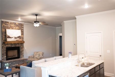 Kitchen with ceiling fan, crown molding, light stone countertops, a brick fireplace, and sink