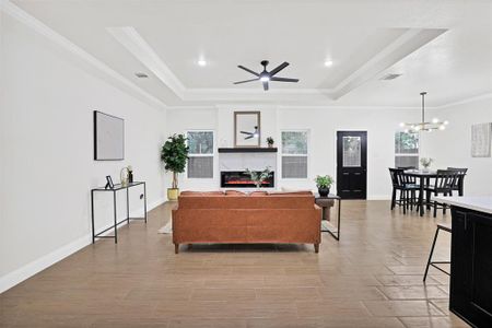 Living room featuring ornamental molding, ceiling fan with notable chandelier, a raised ceiling, and a healthy amount of sunlight