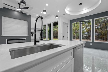 Kitchen with light stone counters, stainless steel dishwasher, ceiling fan, sink, and white cabinets