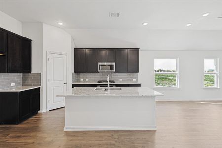 Kitchen featuring decorative backsplash, light hardwood / wood-style floors, and an island with sink