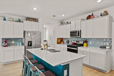 Kitchen with light hardwood / wood-style flooring, backsplash, a kitchen island with sink, white cabinets, and appliances with stainless steel finishes