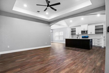 Kitchen with a tray ceiling, a kitchen island with sink, white cabinets, and dark hardwood / wood-style floors