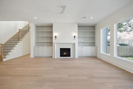 This stunning living room features a harmonious blend of style and functionality. Anchored by a sleek gas fireplace with a minimalist surround, the space exudes warmth and elegance. Flanking the fireplace are custom built-ins with open shelving and lower cabinets, offering both display and storage options.  A staircase with wood treads and iron balusters adds a touch of sophistication, seamlessly connecting this inviting space to the rest of the home.