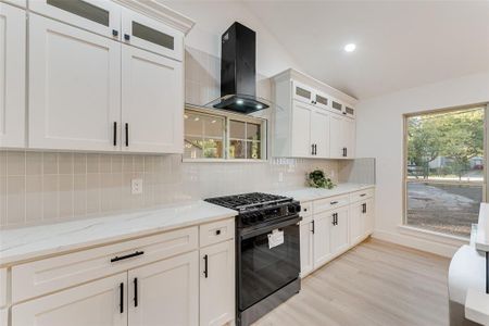 Kitchen featuring light stone countertops, black gas stove, backsplash, island exhaust hood, and lofted ceiling