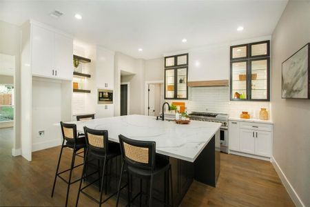 Kitchen with a kitchen island with sink, high end stainless steel range oven, tasteful backsplash, light stone countertops, and white cabinets