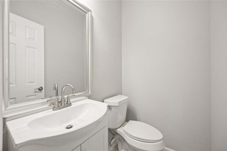 This photo shows a modern, compact bathroom with a sleek white sink, a toilet, and a large mirror. The walls are painted a light, neutral color, enhancing the bright, clean feel of the space.