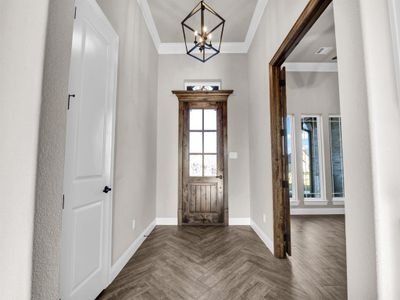 Entryway with a chandelier, dark parquet flooring, and ornamental molding