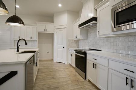 Kitchen featuring light hardwood / wood-style floors, custom range hood, appliances with stainless steel finishes, sink, and tasteful backsplash