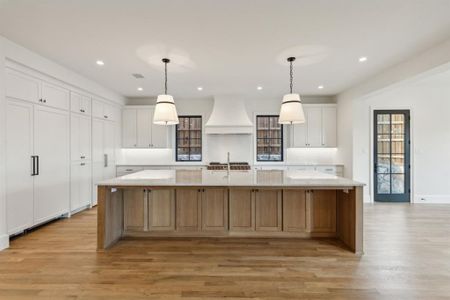 Kitchen featuring white cabinets, pendant lighting, a large island, light hardwood / wood-style flooring, and custom range hood