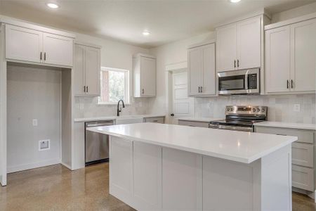 Kitchen featuring appliances with stainless steel finishes, decorative backsplash, white cabinetry, and a center island