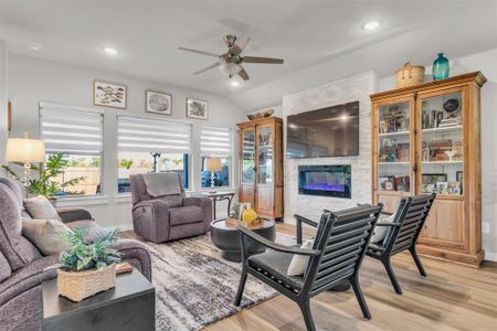 Living room featuring a fireplace, light hardwood / wood-style floors, vaulted ceiling, and ceiling fan