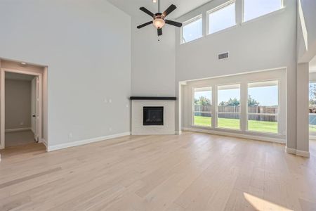 Unfurnished living room featuring ceiling fan, light hardwood / wood-style flooring, and a towering ceiling