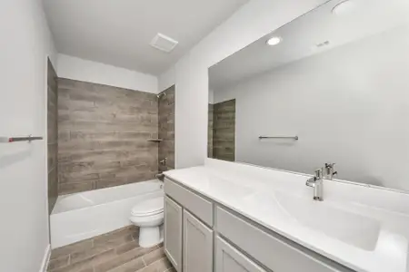 Secondary bath features tile flooring, bath/shower combo with tile surround, light stained wood cabinets, beautiful light countertop.