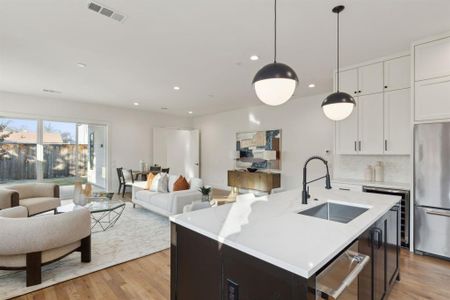 Kitchen featuring stainless steel appliances, sink, white cabinets, an island with sink, and hanging light fixtures