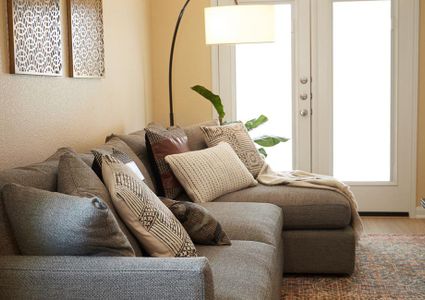 A living room decorated with a comfortable, gray couch with tan accents, a large floor lamp, and French doors that lead to the large backyard.